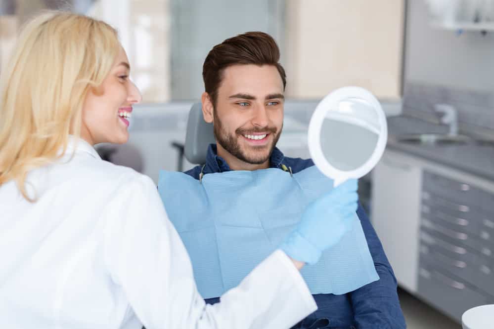 Cheerful woman doctor holding mirror for happy man patient - stock image